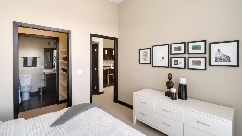 Modern bedroom with a white dresser, framed art, and open doorways to a bathroom and another room.