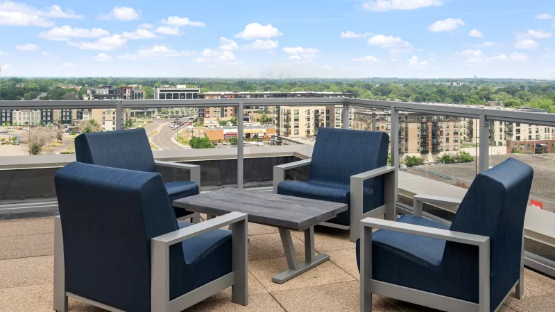Rooftop patio with four modern blue chairs, a grey table, and a city skyline under a blue sky.