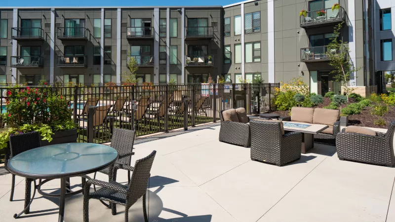 Modern apartment complex patio with pool, fire pit, and outdoor furniture. Sunny day.