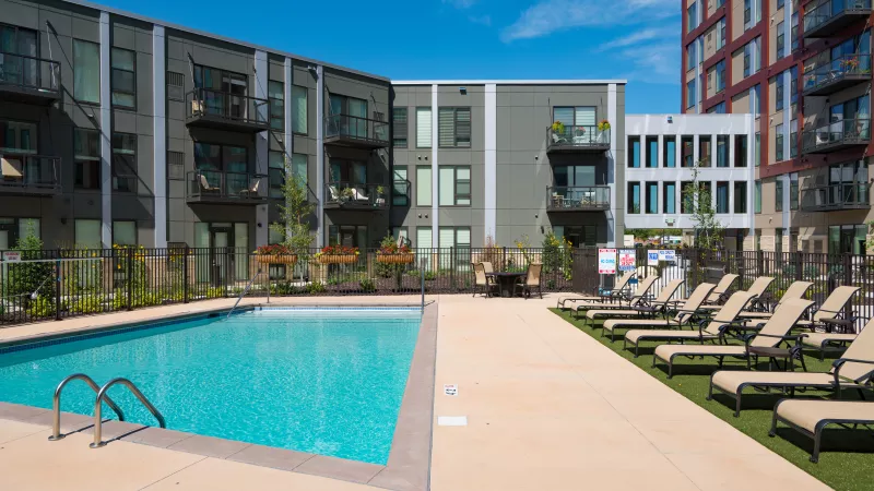 Outdoor swimming pool and lounge chairs at a modern apartment complex under a clear blue sky.