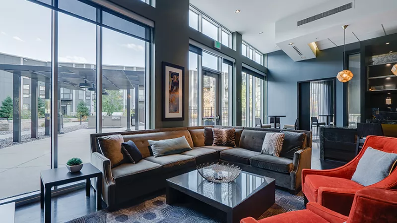 Modern lounge with L-shaped sofa, orange chairs, and large windows overlooking an outdoor patio.