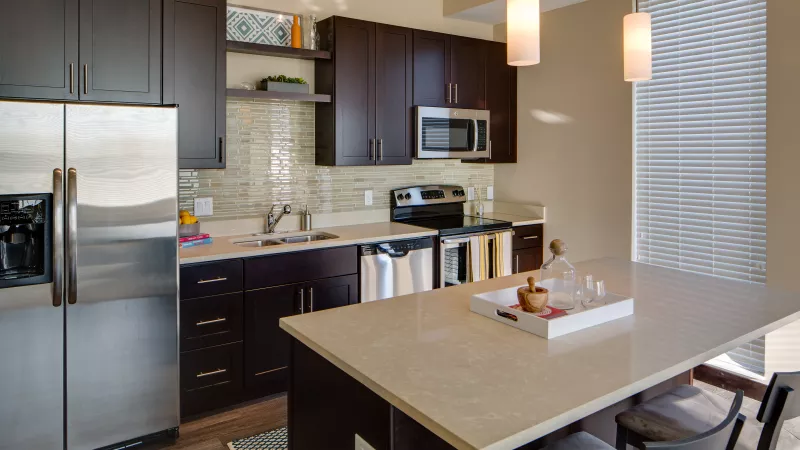 Modern kitchen with dark cabinets, stainless steel appliances, light countertops, and an island with bar stools.