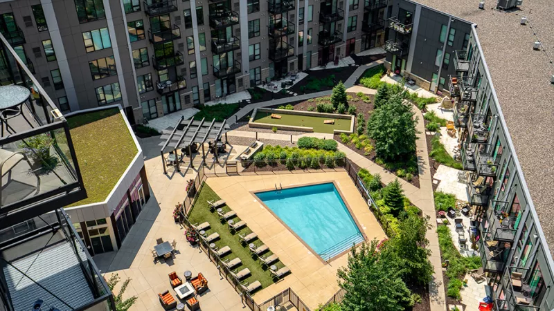 Aerial view of a modern apartment complex courtyard with a triangular pool, lounge chairs, mini-golf, and green spaces.