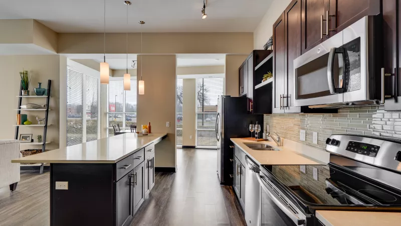Modern kitchen with dark wood cabinets, light countertops, stainless steel appliances, and a central island.