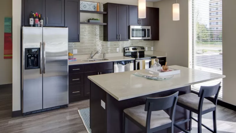 Modern kitchen with dark cabinets, stainless steel appliances, light countertops, and an island with bar stools.