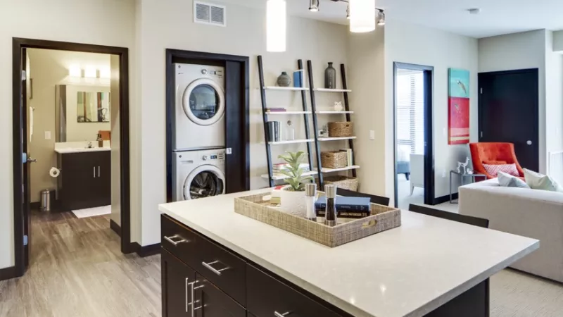 Modern apartment interior featuring a kitchen island, stacked washer/dryer, bathroom, and living room.