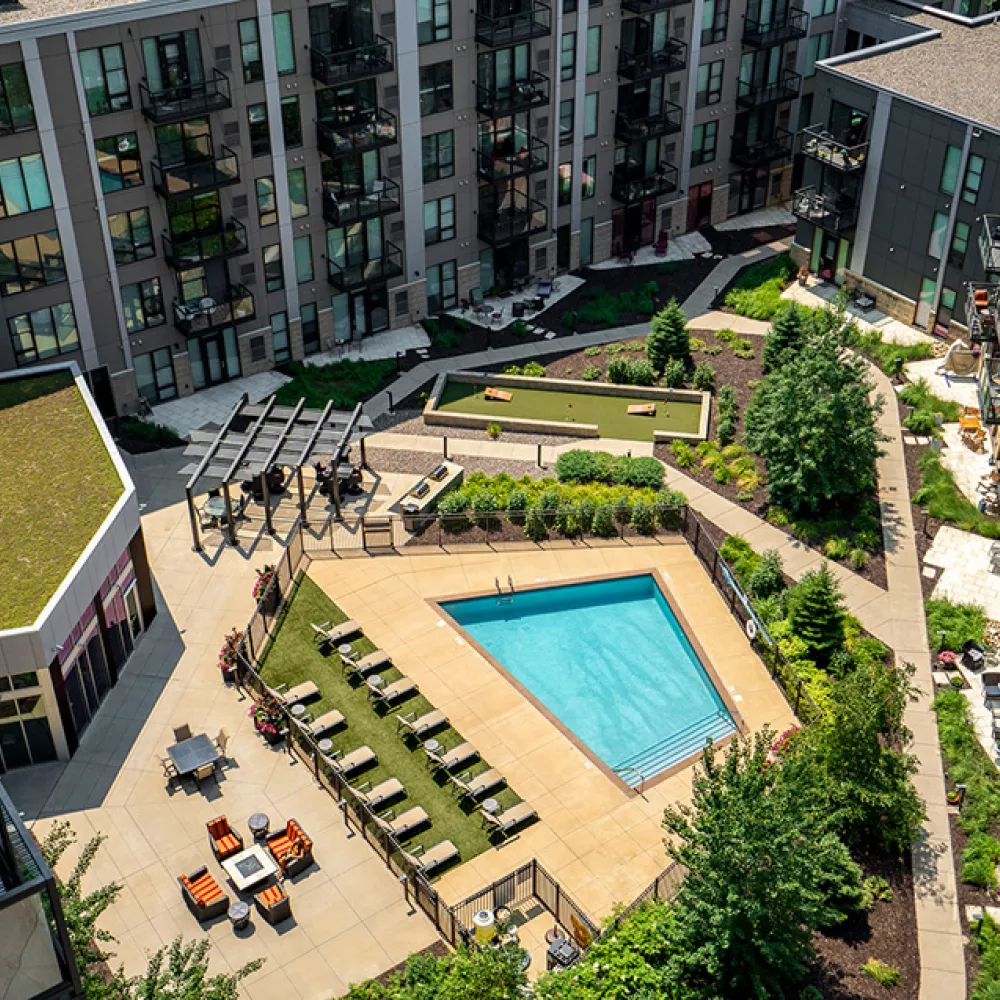 High-angle view of a modern apartment complex courtyard with a triangular pool, putting green, green roof, and balconies.