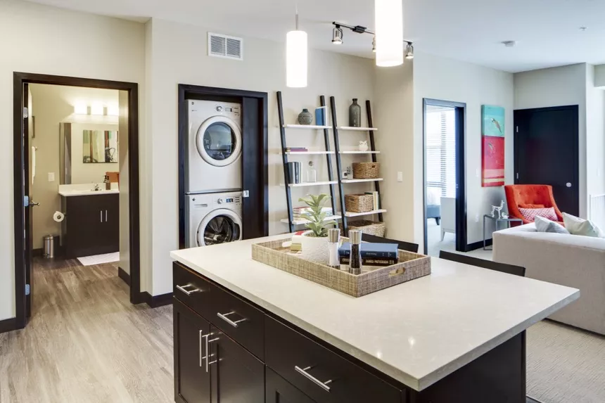 Modern apartment interior featuring a kitchen island, stacked washer/dryer, bathroom, and living room.